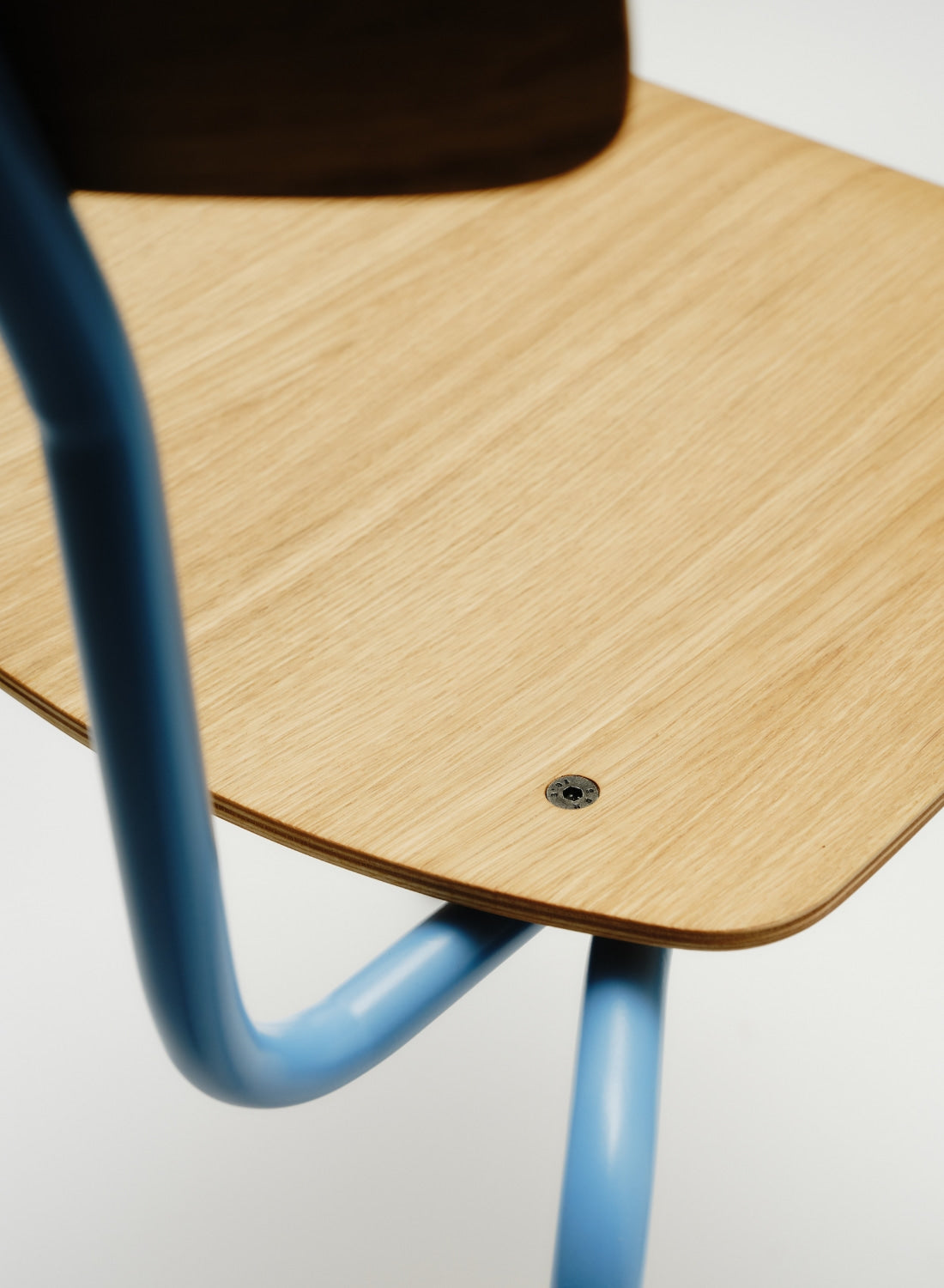 Detailaufnahme des B01 Design-Holzstuhls von Bensberger mit hochwertiger Sitzfläche aus Eichenholz und farbig pulverbeschichtetem Stahlrohrgestell in Pastellblau.